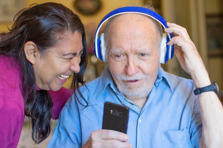 older man listening to a song on headphones smiling with carer